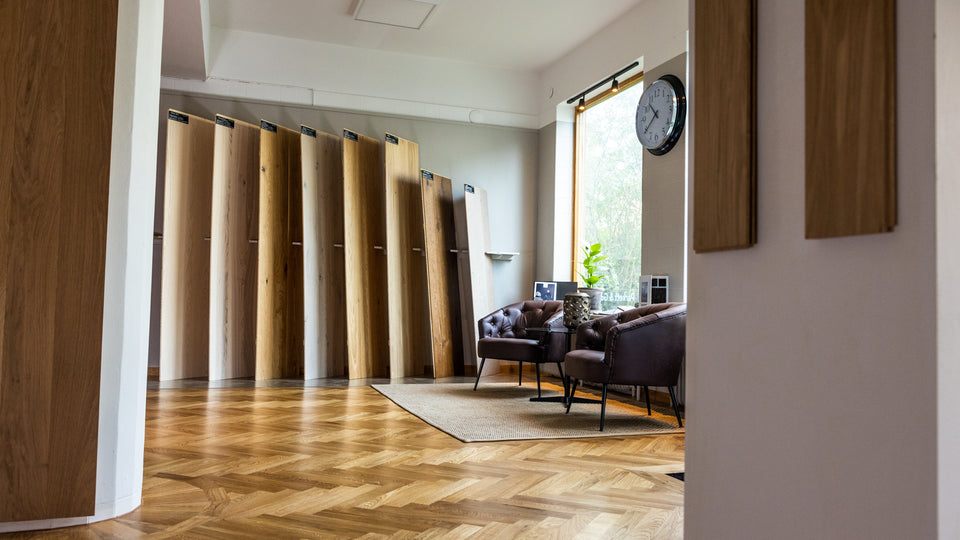 Bred vy av showroom med stående provskivor längs väggen och fiskbensgolv i lokalen.